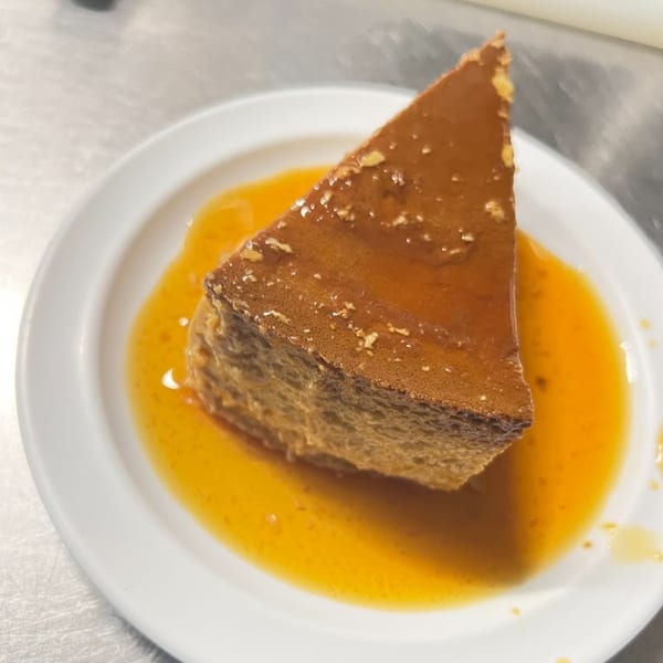A slice of Mexican flan with caramel sauce on a white plate.