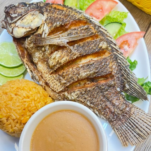 Whole fried fish with rice, limes, and a side salad with tomatoes and cucumbers.