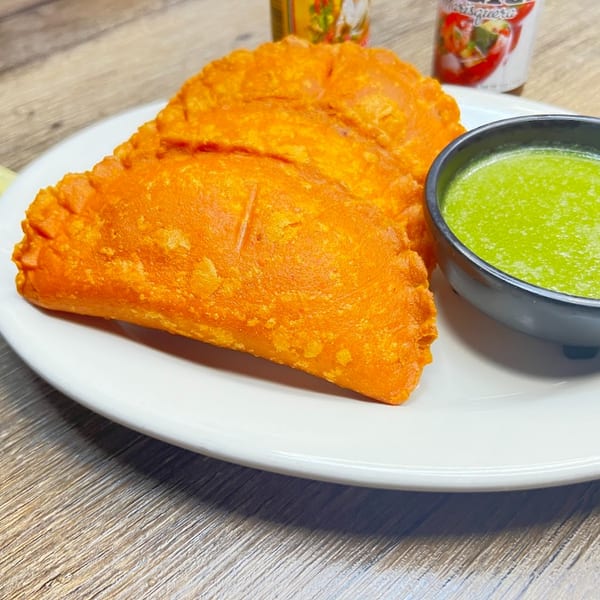 Two golden-orange empanadas and a small black bowl of green sauce on a white plate.