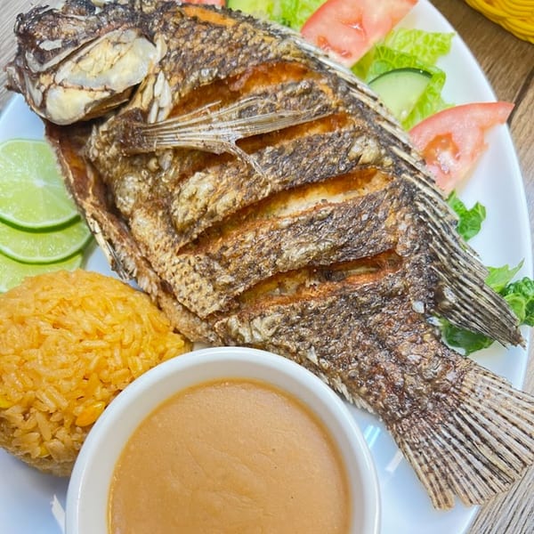 A whole fried fish with rice, lime slices, salad, and a small bowl of sauce.