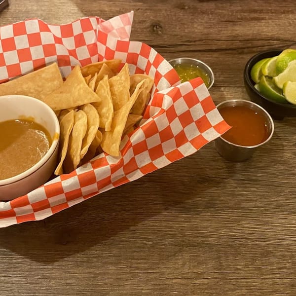 Basket of tortilla chips with a bowl of birria consommé, salsa, and lime wedges on a wooden table.