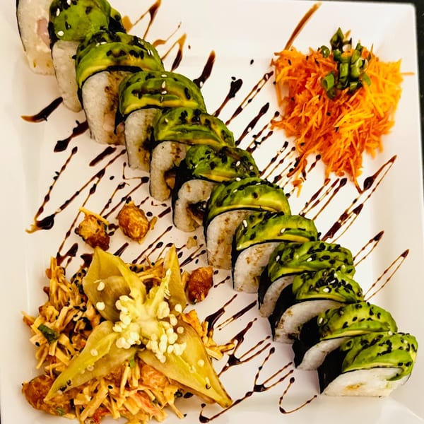 Avocado-topped sushi rolls with sesame seeds, shredded carrots, and a side salad on a white plate.